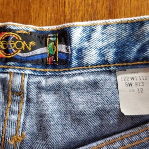 May include: Light blue denim shorts with a faded look. The shorts have a brown leather patch with the word "JASON" in white lettering. The size tag reads "122 W1 1127 SW 913 Size 12".