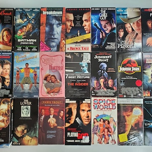 May include: A collection of VHS tapes featuring movie titles like "Batman Forever," "Jurassic Park," and "Spice World." The tapes have colorful covers with various actors and movie titles. The collection includes a variety of genres, from action to drama.
