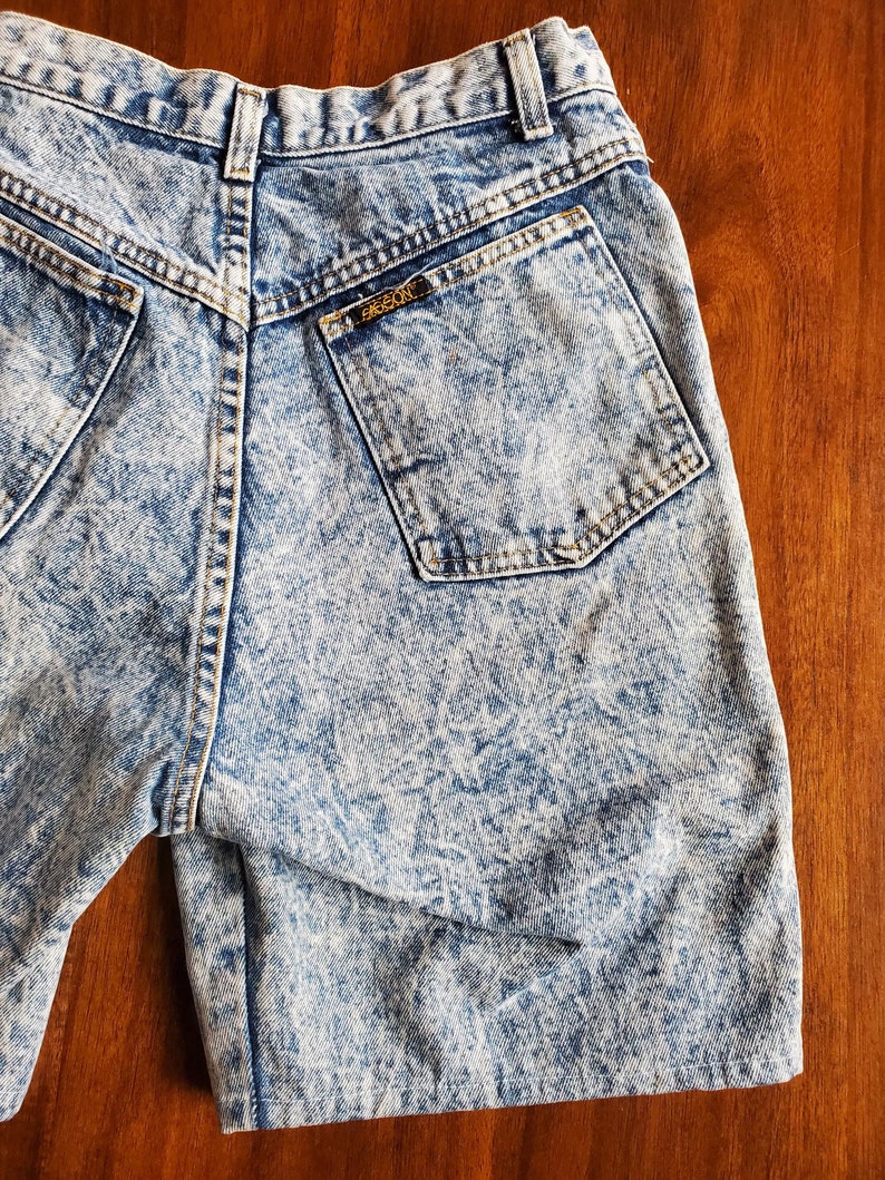 May include: Light blue acid wash denim shorts with a back pocket that has a brown leather label with the text "FRESCO" on it.