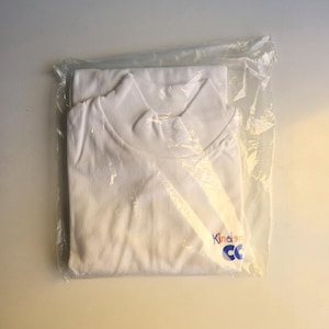 May include: A white turtleneck shirt, folded and sealed in a clear plastic bag. The shirt has a small logo in blue and red on the front. The shirt is made of a soft material.