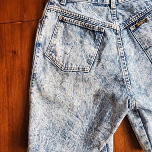 May include: Light blue acid wash denim shorts with a back pocket and a gold logo label.