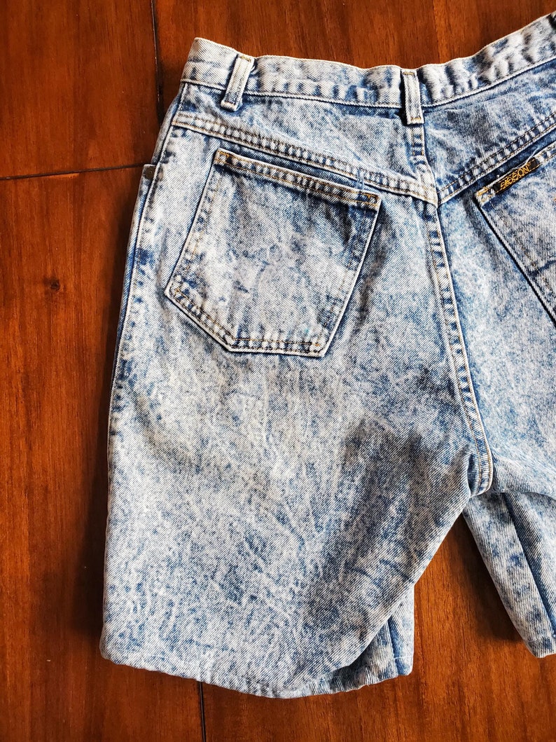 May include: Light blue acid wash denim shorts with a back pocket and a gold logo label.