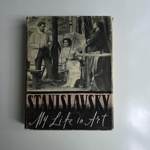 Può includere: Un libro d'epoca intitolato "STANISLAVSKY My Life in Art". La copertina presenta una fotografia in bianco e nero di tre persone, una con un ombrello. Il libro ha un aspetto usurato, che suggerisce età e utilizzo.