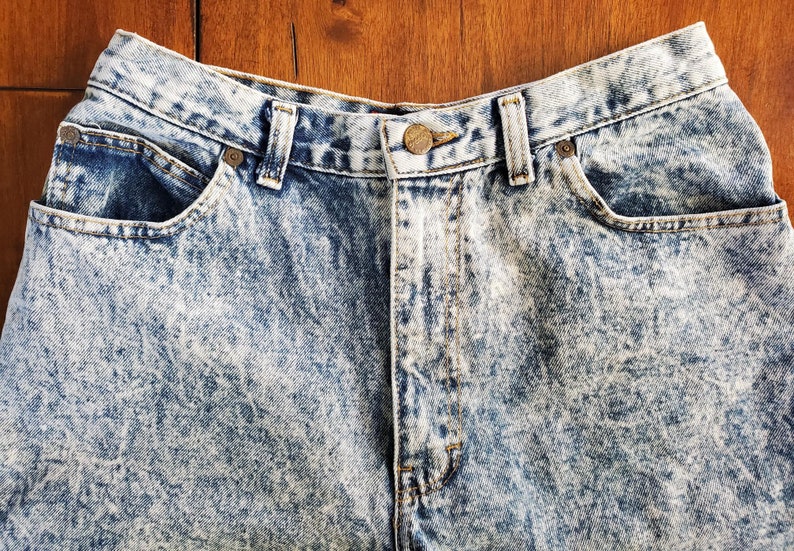 May include: A pair of light blue acid wash denim jeans with a button fly and five pockets.