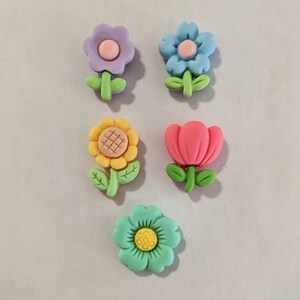 May include: Five colorful flower-shaped buttons with a variety of designs, including a sunflower, a tulip, and three different types of flowers.