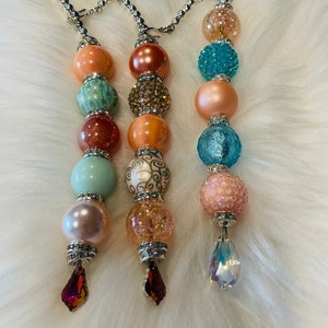 May include: Three beaded keychains with crystal drops. Each keychain features a different color scheme: peach, teal, and pink. The beads are a mix of smooth, textured, and sparkly.