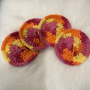 May include: Four crocheted coasters in a swirl pattern of pink, orange, and yellow.