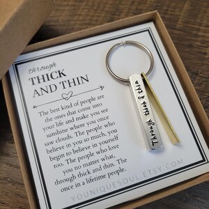 May include: A silver keychain with the words "Through Thick & Thin" engraved on it. The keychain is in a small box with a card that reads "The best kind of people are the ones that come into your life and make you see sunshine where you once saw clouds. The people who believe in you so much, you begin to believe in yourself too. The people who love you no matter what, through thick and thin. The once in a lifetime people."