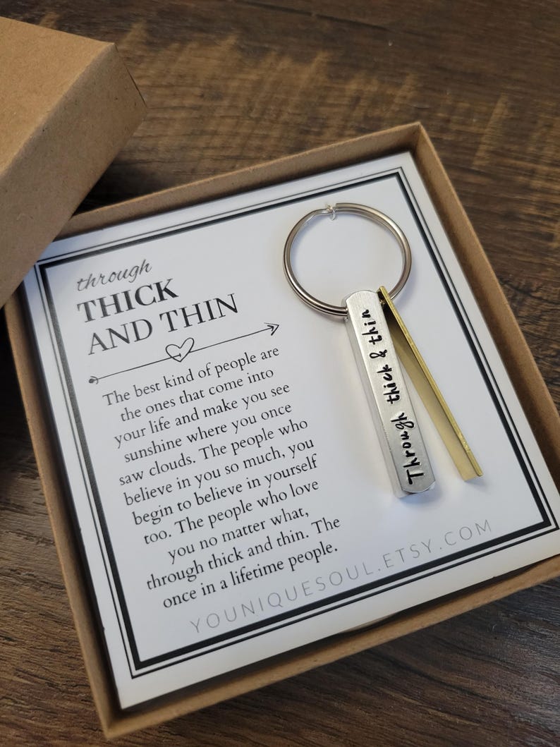 May include: A silver keychain with the words "Through Thick & Thin" engraved on it. The keychain is in a small box with a card that reads "The best kind of people are the ones that come into your life and make you see sunshine where you once saw clouds. The people who believe in you so much, you begin to believe in yourself too. The people who love you no matter what, through thick and thin. The once in a lifetime people."