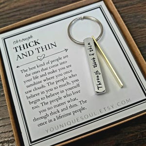 May include: A silver keychain with a bar charm engraved with the words "Through thick & thin". The keychain is displayed on a white card with a message about the importance of true friends. The card also includes the Etsy shop name "Youniquessoul.etsy.com".
