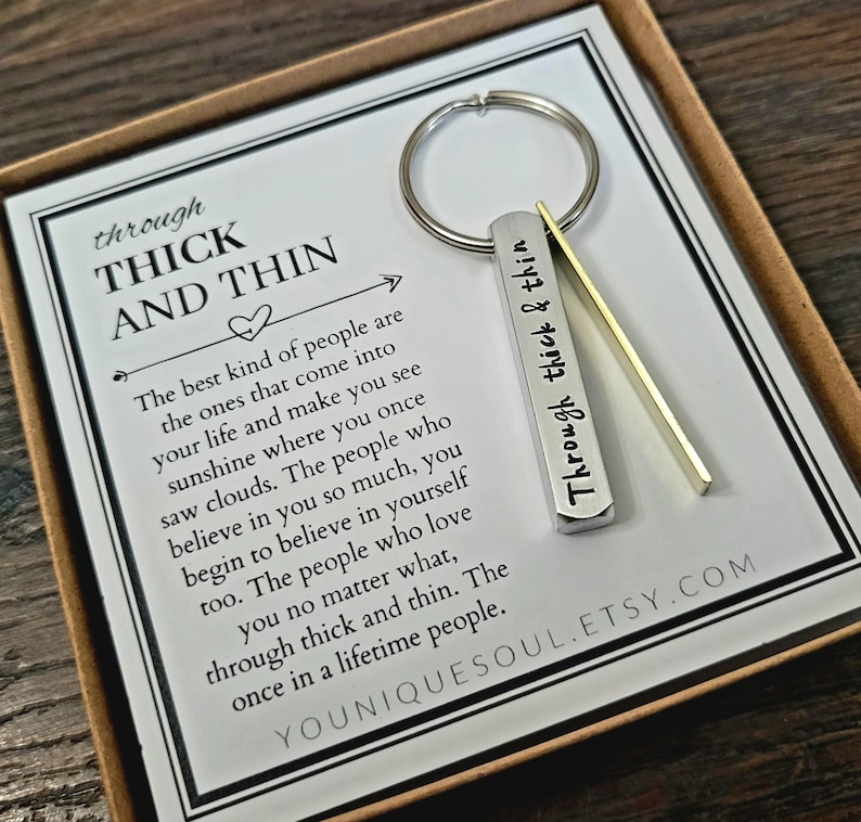 May include: A silver keychain with a bar charm engraved with the words "Through thick & thin". The keychain is displayed on a white card with a message about the importance of true friends. The card also includes the Etsy shop name "Youniquessoul.etsy.com".