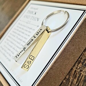 May include: A silver and gold keychain with a silver bar engraved with the words "Through thick & thin" and the initials "S&B". The keychain is in a brown box with the words "Thick and Thin" printed on the inside.