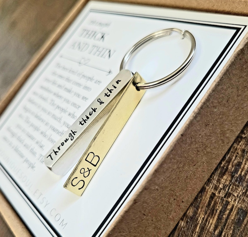 May include: A silver and gold keychain with a silver bar engraved with the words "Through thick & thin" and the initials "S&B". The keychain is in a brown box with the words "Thick and Thin" printed on the inside.