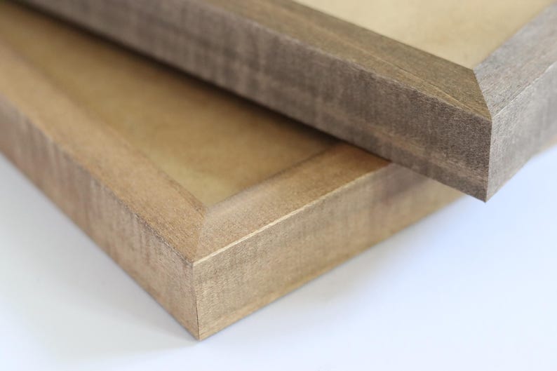 May include: Two wooden picture frames, one on top of the other. The top frame is a darker brown wood with a smooth finish. The bottom frame is a lighter brown wood with a more textured finish.