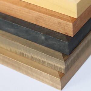 May include: A stack of five wooden picture frames in various shades of brown, from light to dark.