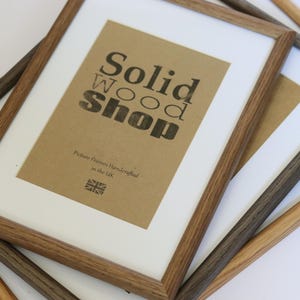 Puede incluir: Tres marcos de fotos de madera en diferentes tonos de marr&oacute;n. El marco m&aacute;s grande tiene un inserto de papel marr&oacute;n con el texto "Solid Wood Shop" y "Picture Frames Handcrafted in the UK".