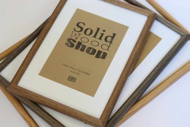Puede incluir: Tres marcos de fotos de madera en diferentes tonos de marr&oacute;n. El marco m&aacute;s grande tiene un inserto de papel marr&oacute;n con el texto "Solid Wood Shop" y "Picture Frames Handcrafted in the UK".