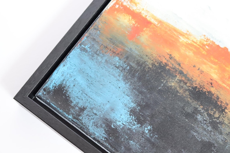 May include: Abstract art piece with a black frame. The artwork features a blend of colors, including orange, blue, and gray, creating a textured, layered effect. The painting is mounted in a dark wooden frame, adding a modern touch.