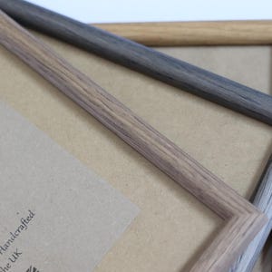 Puede incluir: Dos marcos de fotos de madera, uno marr&oacute;n claro y otro gris oscuro, est&aacute;n apilados uno encima del otro. Los marcos est&aacute;n hechos de madera real y tienen un patr&oacute;n de veta natural. Los marcos est&aacute;n vac&iacute;os y listos para usarse para mostrar fotos u obras de arte.