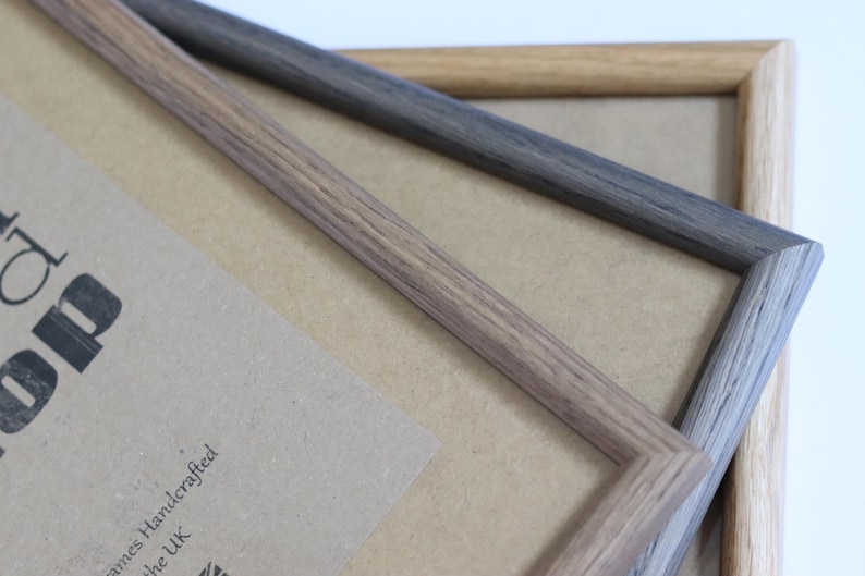 Puede incluir: Dos marcos de fotos de madera, uno marr&oacute;n claro y otro gris oscuro, est&aacute;n apilados uno encima del otro. Los marcos est&aacute;n hechos de madera real y tienen un patr&oacute;n de veta natural. Los marcos est&aacute;n vac&iacute;os y listos para usarse para mostrar fotos u obras de arte.