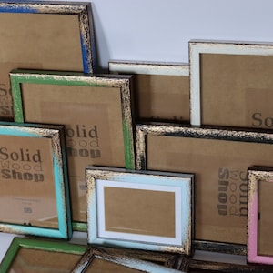 May include: Assortment of rustic wooden picture frames in various sizes and colors, including blue, green, pink, and black. The frames have a distressed finish and gold accents. The frames are all labeled with the text "Solid Wood Shop".