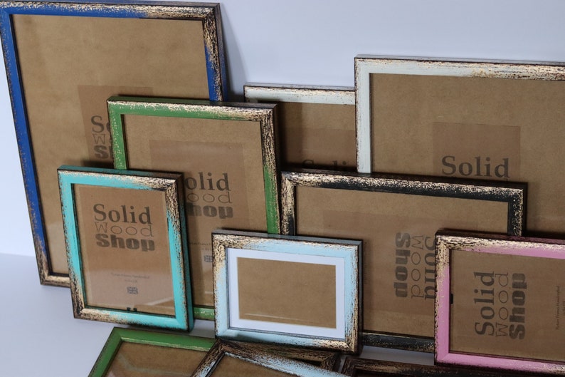 May include: Assortment of rustic wooden picture frames in various sizes and colors, including blue, green, pink, and black. The frames have a distressed finish and gold accents. The frames are all labeled with the text "Solid Wood Shop".