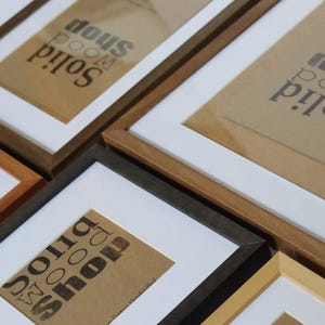 May include: Four different picture frames with a white mat and a brown paper insert with the text "Solid Wood Room Shop" printed in black. The frames are made of wood and come in different colors, including natural wood, dark brown, black, and light brown.