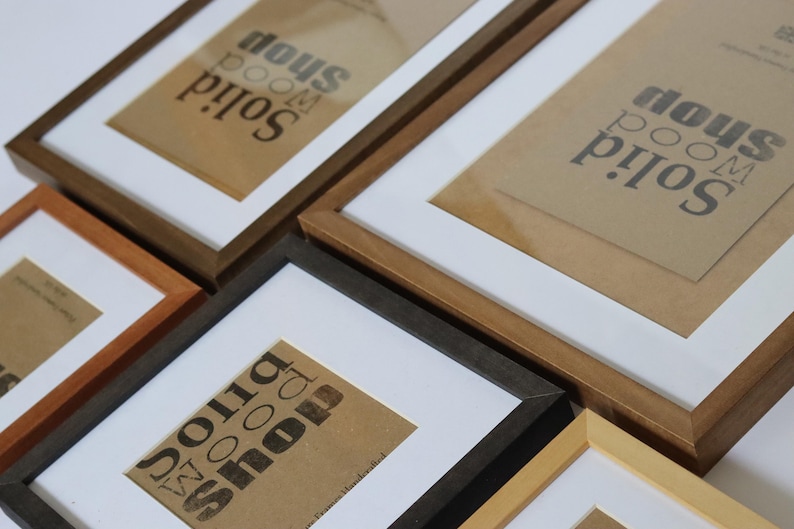 May include: Four different picture frames with a white mat and a brown paper insert with the text "Solid Wood Room Shop" printed in black. The frames are made of wood and come in different colors, including natural wood, dark brown, black, and light brown.