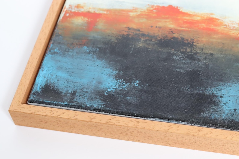 May include: Abstract art piece with a wooden frame. The artwork features a textured surface with layers of color, including orange, blue, black, and white. The painting has a modern aesthetic.