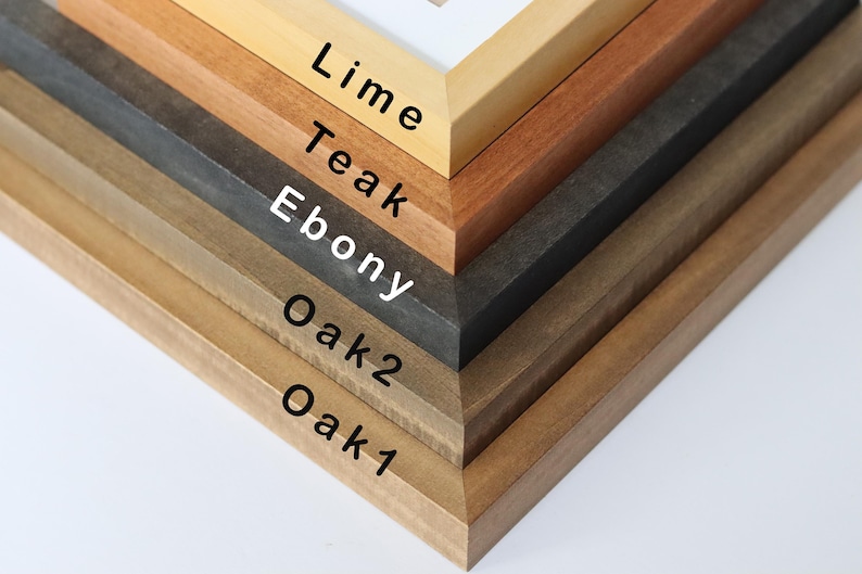 May include: Close-up of six different wood picture frames stacked on top of each other. The frames are labeled from bottom to top: Oak 1, Oak 2, Ebony, Teak, Lime.