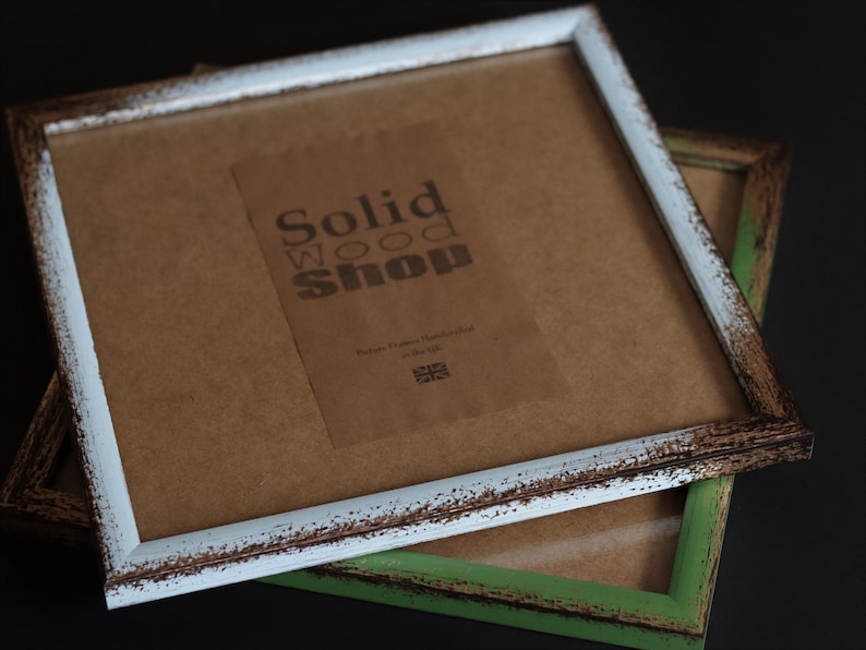 May include: Two rustic picture frames, one with a white distressed finish and the other with a green distressed finish. The white frame has a label that reads "Solid Wood Shop, Picture Frames Handcrafted in the UK".