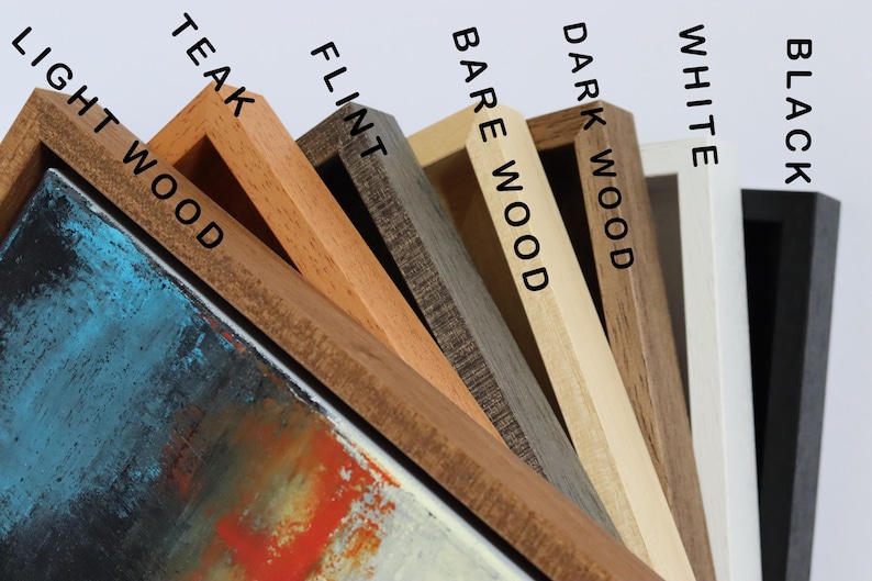 May include: Close-up of a selection of wooden picture frames in various colors, including light wood, teak, flint, bare wood, dark wood, white, and black. The frames are angled, showcasing the different wood tones and textures. The text on the frames indicates the color.