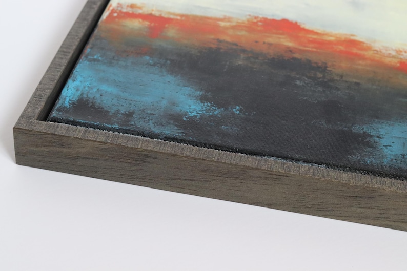 May include: Abstract art piece with a dark gray wooden frame. The canvas features a textured surface with a blend of colors, including black, blue, orange, and white. The artwork is a close-up view, showcasing the details of the paint.