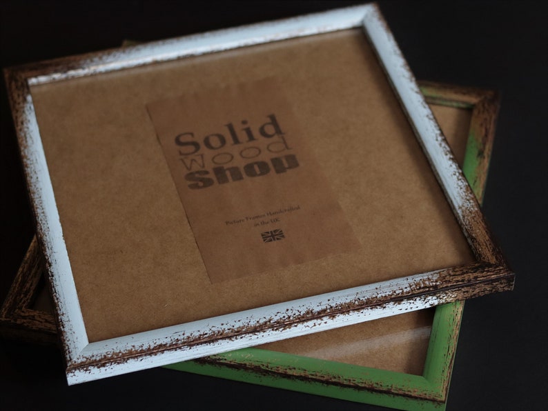 May include: Two rustic picture frames, one with a white distressed finish and the other with a green distressed finish. The white frame has a brown paper backing with a label that reads "Solid Wood Shop, Picture Frames Handcrafted in the UK".