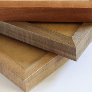 May include: Three wooden picture frames stacked on top of each other. The top frame is a light brown wood, the middle frame is a dark brown wood, and the bottom frame is a light brown wood.