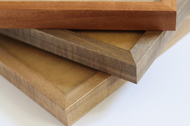 May include: Three wooden picture frames stacked on top of each other. The top frame is a light brown wood, the middle frame is a dark brown wood, and the bottom frame is a light brown wood.