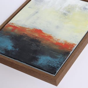 May include: Abstract landscape painting with a wooden frame. The artwork features a textured surface with layers of color, including white, yellow, red, blue, and black. The painting is a modern piece of art.