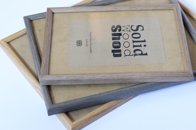 Puede incluir: Dos marcos de fotos de madera apilados uno encima del otro. El marco superior es de madera marr&oacute;n claro con un paspart&uacute; blanco y el texto "Solid Wood Shop" impreso en el paspart&uacute;. El marco inferior es de madera gris oscuro con un paspart&uacute; blanco.