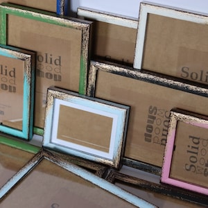 May include: Assortment of colorful picture frames with distressed wood finishes. The frames are various sizes and feature a gold-colored trim. The frames are stacked on top of each other and some have the text "Solid Wood Shop" printed on them.