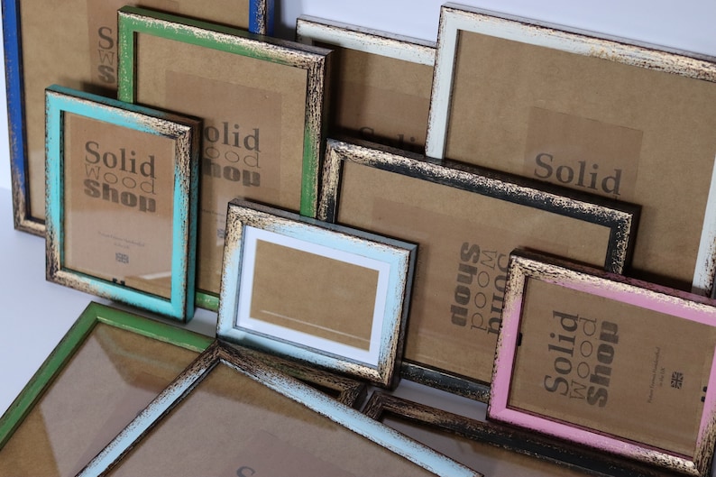 May include: Assortment of colorful picture frames with distressed wood finishes. The frames are various sizes and feature a gold-colored trim. The frames are stacked on top of each other and some have the text "Solid Wood Shop" printed on them.