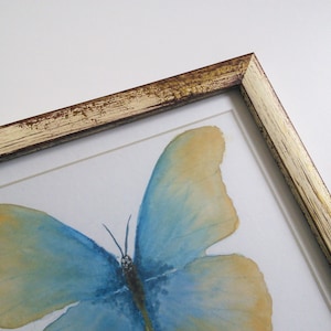 May include: A framed watercolor painting of a blue and yellow butterfly with a distressed gold frame.