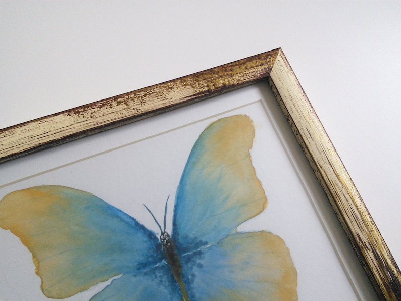 May include: A framed watercolor painting of a blue and yellow butterfly with a distressed gold frame.