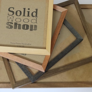 May include: Four wooden picture frames stacked on top of each other. The top frame is light brown and has the text "Solid Wood Shop" printed on it. The other frames are darker brown and have a natural wood finish.