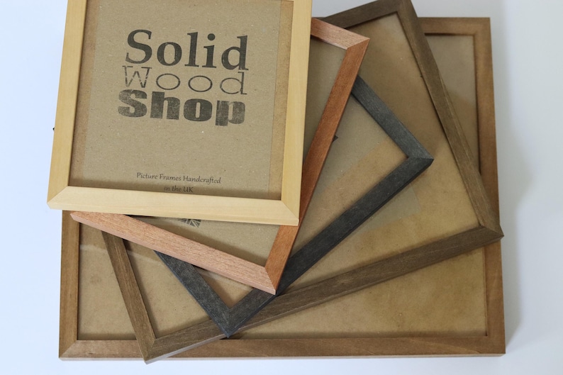 May include: Four wooden picture frames stacked on top of each other. The top frame is light brown and has the text "Solid Wood Shop" printed on it. The other frames are darker brown and have a natural wood finish.