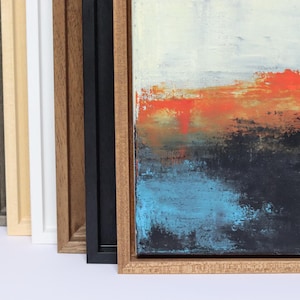 May include: Abstract artwork with a textured surface, showcasing orange, black, and blue hues. The piece is presented in a natural wood frame, with other frame colours visible in the background. The frames are made of wood.