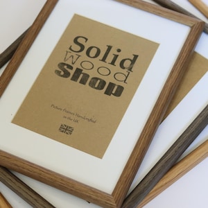 May include: Three wooden picture frames in different shades of brown. The largest frame has a brown paper insert with the text "Solid Wood Shop" and "Picture Frames Handcrafted in the UK".