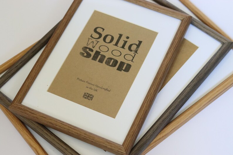 May include: Three wooden picture frames in different shades of brown. The largest frame has a brown paper insert with the text "Solid Wood Shop" and "Picture Frames Handcrafted in the UK".