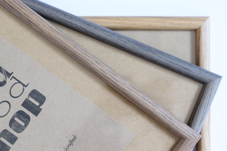 Puede incluir: Dos marcos de fotos, uno marr&oacute;n claro y otro gris oscuro, est&aacute;n apilados uno encima del otro. Los marcos son de madera y tienen un dise&ntilde;o simple y cl&aacute;sico.
