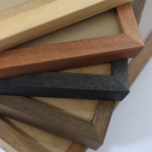 May include: Close-up of four picture frames stacked on top of each other. The top frame is light wood, the second is reddish brown, the third is black, and the bottom frame is dark brown.