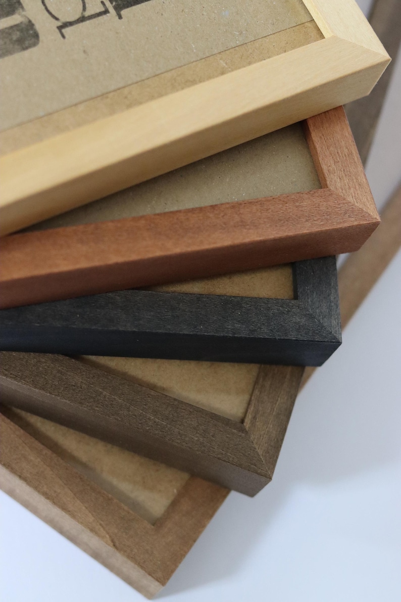 May include: Close-up of four picture frames stacked on top of each other. The top frame is light wood, the second is reddish brown, the third is black, and the bottom frame is dark brown.